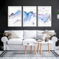 Three framed art prints with watercolour mountain landscapes displayed above a white sofa in a modern living room.