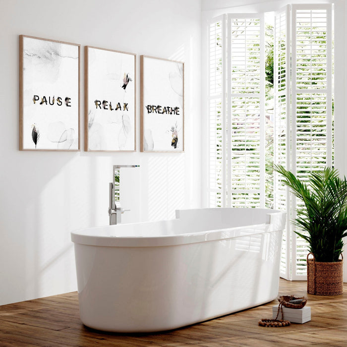 Modern bathroom artwork triptych displaying 'Pause, Relax, Breathe' with minimalist botanical designs above a contemporary white freestanding bathtub.