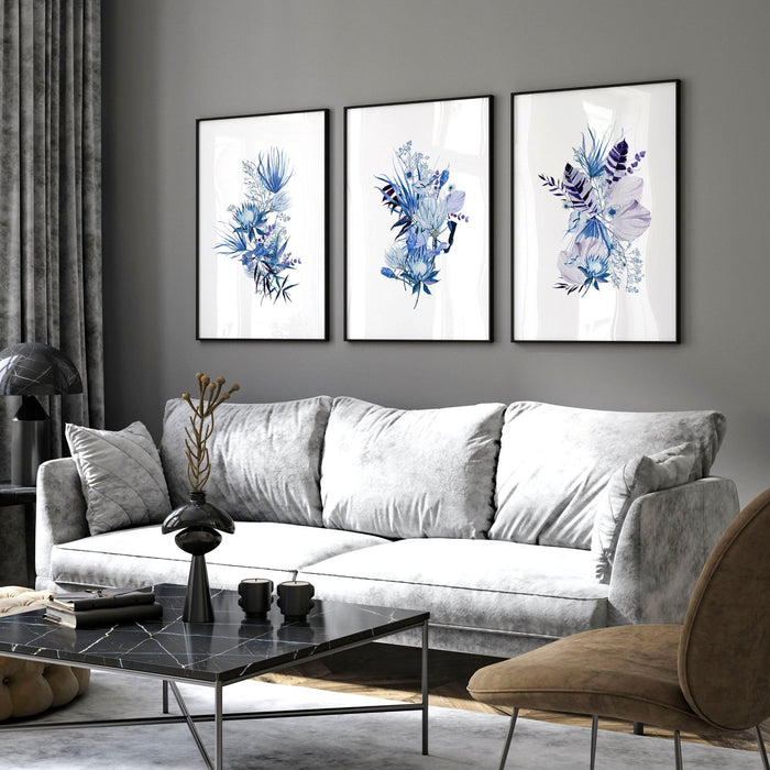 Three framed botanical wall art prints with blue flowers displayed above a grey sofa in a modern living room
