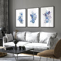 Three framed botanical wall art prints with blue flowers displayed above a grey sofa in a modern living room