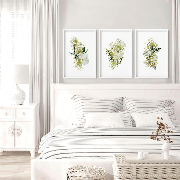 Three white-framed botanical prints displayed as framed wall art for bedroom above a striped bed