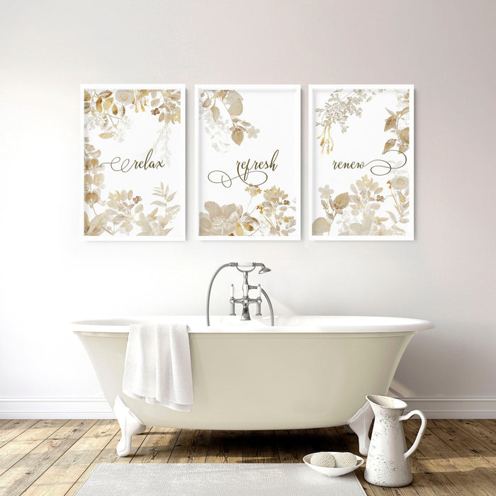 Three framed gold botanical prints displaying relax, refresh and renew above a freestanding bathtub